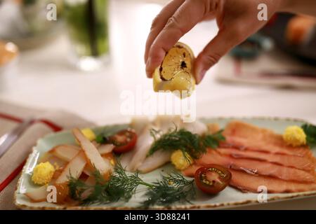 Une main presse le citron sur un plateau de fruits de mer magnifiquement arrangé avec divers poissons, herbes et garnitures. L'atmosphère est accueillante et détendue Banque D'Images