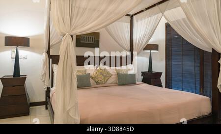 Un lit avec un baldaquin et draps blancs. Le lit est recouvert d'oreillers et d'une couverture blanche Banque D'Images