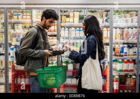 Femme magasinant le carton de lait avec un ami masculin à la section réfrigérée dans le supermarché Banque D'Images