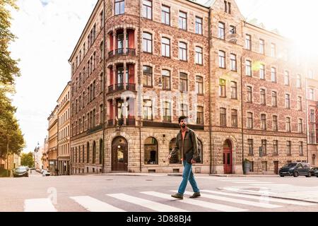 Pleine longueur de l'homme traversant la route sur la rue à la journée ensoleillée Banque D'Images