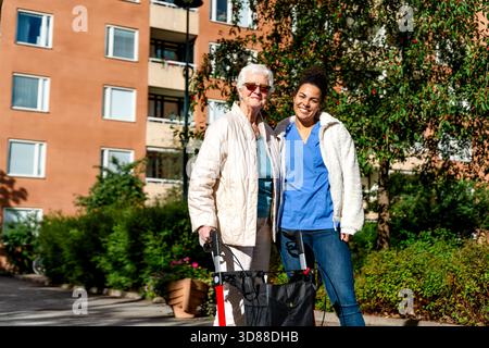 Portrait d'une infirmière souriante debout avec une femme âgée dans le parc à la journée ensoleillée Banque D'Images