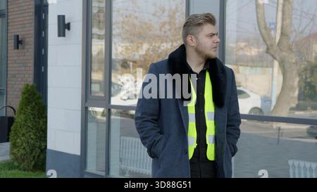 Un ouvrier dans un gilet réfléchissant debout à l'extérieur près d'un chantier de construction Banque D'Images