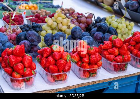 Bol de fruits en vente sur le marché alimentaire. Nourriture vitaminée. Baies rouges et bleues. Prune, raisins et fraises ensemble différent Banque D'Images