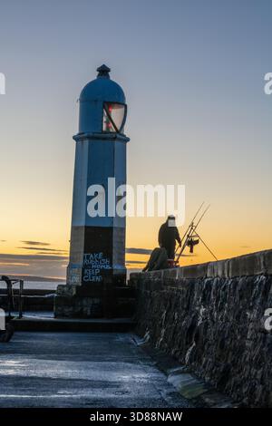 Pêcheur à l'aube à côté du phare de Porthcawl sur la jetée alors que la première lumière se brise au-dessus de l'horizon, pays de Galles du Sud Banque D'Images