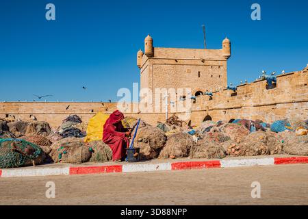 Pêcheur marocain reposant avec chat orange sur des filets de pêche près des murs de la forteresse d'Essaouira Banque D'Images