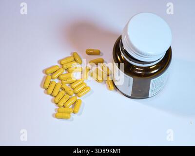 Capsules jaunes et flacon de médicament - gros plan de capsules jaunes renversées d'un flacon de médicament brun sur une surface blanche propre. Idéal pour les soins de santé, Banque D'Images