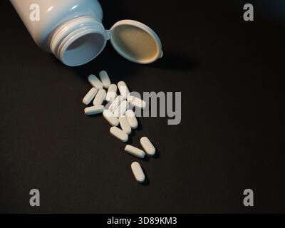 Pilules renversées de Open Medicine Bottle - Une dispersion de pilules ovales blanches, beaucoup marquées IH25, sont tombées d'une bouteille de médecine en plastique blanc ouvert o Banque D'Images