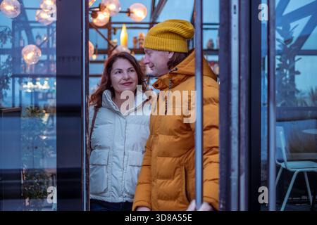 Midlife couple profite d'une soirée confortable dans un café élégant, entouré d'un éclairage chaleureux et d'une ambiance détendue, partageant des moments joyeux et connexion Banque D'Images