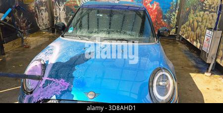 Berlin, Allemagne - 27 septembre 2025 : Mini Cooper est lavé dans un lave-auto avec une murale sous-marine vibrante. Banque D'Images