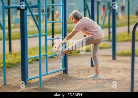 Femme senior faisant l'exercice d'étirement de jambe sur l'échelle. Vue corps entier. Banque D'Images