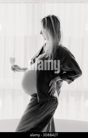 34 semaine, une femme enceinte pose soigneusement dans une pièce ensoleillée, mettant en valeur la féminité et l'anticipation calme. Environnement minimal et tons délicats Banque D'Images