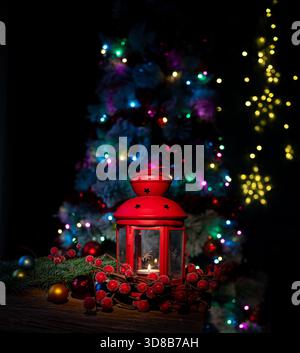 Lanterne rouge avec bougie et décorations de Noël devant un arbre éclairé Banque D'Images