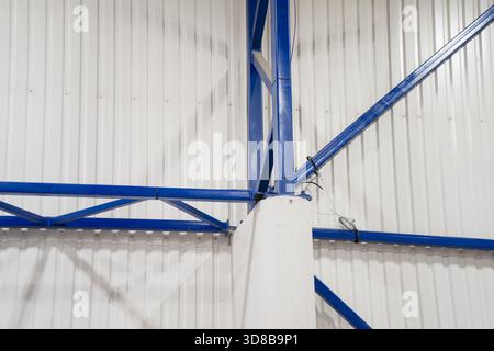 Fermes de toit en acier bleu et colonne de support à l'intérieur du bâtiment industriel, montrant l'ossature structurelle et les panneaux muraux métalliques dans l'intérieur moderne de l'entrepôt Banque D'Images