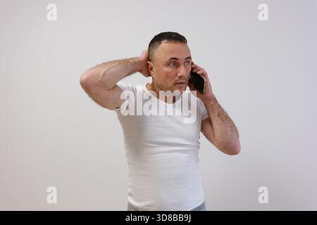 Homme d'affaires d'âge moyen confus, gestionnaire d'homme d'affaires professionnel plus âgé portant costume à l'aide d'un téléphone portable regardant le message de lecture de smartphone sur le téléphone portable debout isolé sur blanc. Banque D'Images