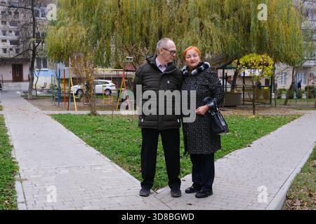 Hommes adultes et femme assis sur un banc famille de couple retraité caucasien dans l'amour femme mature homme assis sur le banc ensemble souriant épouse mari conjoints nouvelles vieillesse et smartphone dans la ville à l'extérieur. Banque D'Images