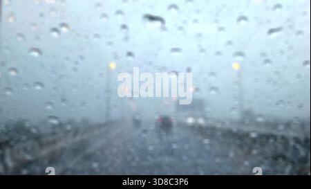 Image floue de gouttes de pluie sur le pare-brise d'une voiture un jour de pluie sur une autoroute. Banque D'Images