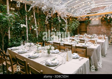 Les tables sont magnifiquement disposées avec des fleurs blanches et des décorations dans un cadre de jardin charmant, parfait pour les rassemblements. Banque D'Images