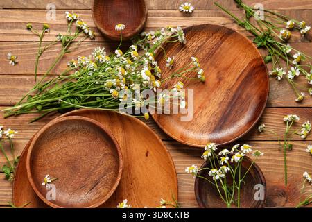 Composition avec différentes assiettes et fleurs de camomille fraîches sur fond en bois Banque D'Images
