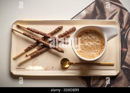 Une scène accueillante avec quelques gressins enrobés de chocolat élégamment disposés à côté d'une tasse de café à la vapeur sur une assiette élégante, apportant comf Banque D'Images