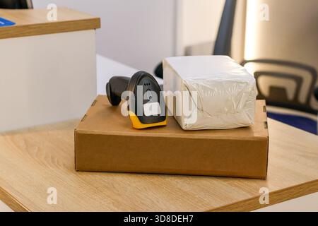Lecteur de code à barres noir à côté du paquet blanc scellé sur la boîte en carton sur le bureau en bois. Banque D'Images