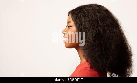 Femme Millennial souriante avec cheveux bouclés dans profil tourné sur un fond lumineux Banque D'Images