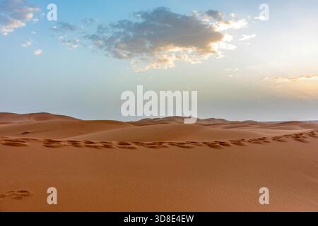 Lumière chaude du soir au-dessus des dunes de sable du désert de l'Erg Chebbi, Maroc, sous un ciel partiellement nuageux Banque D'Images