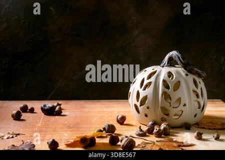 Décorations d'Halloween ou de Thanksgiving, citrouille en céramique sculptée blanche se tenant debout sur une table en pierre orange avec des feuilles d'automne et des glands. Décoration intérieure des fêtes d'Halloween. Copier l'espace Banque D'Images