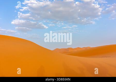 Lumière chaude du soir au-dessus des dunes de sable du désert de l'Erg Chebbi, Maroc, sous un ciel partiellement nuageux Banque D'Images