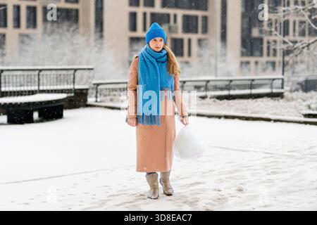 Femme dans un manteau marche à travers la neige dans une cour en hiver. La femme porte un sac poubelle Banque D'Images