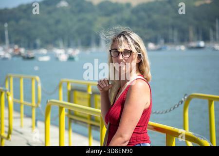 Femme debout sur un ferry ou une jetée regardant à travers un port rempli de bateaux amarrés, illustrant le voyage, la réflexion et le style de vie côtier. Banque D'Images