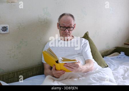 Le vieil homme lit un livre avant d'aller au lit. Lit de lecture vieil homme Banque D'Images