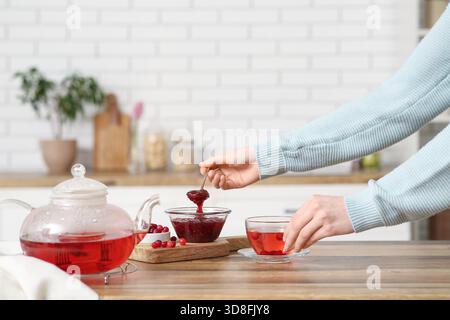 Jeune femme faisant du thé avec de la confiture de canneberges dans la cuisine Banque D'Images