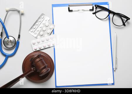 Marteau de juge avec pilules, stéthoscope, presse-papiers vierge et lunettes sur fond clair Banque D'Images