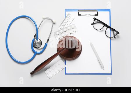 Marteau de juge avec pilules, stéthoscope, presse-papiers et lunettes sur fond clair Banque D'Images