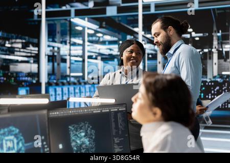 Équipe d'ingénieurs dans le centre de données intégrant des outils d'automatisation pilotés par l'IA, faisant de la maintenance. Collègues travaillant en équipe dans la salle des serveurs utilisant des modèles d'apprentissage automatique d'intelligence artificielle Banque D'Images
