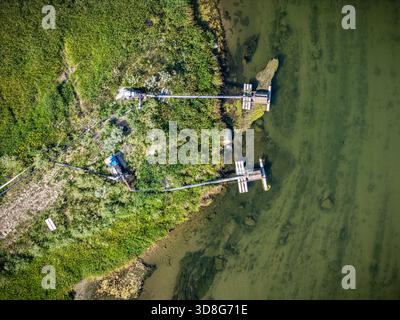 Vue sur un lac avec deux quais et une petite maison en arrière-plan. L'eau est verte et trouble, et le quai est vieux et altéré Banque D'Images
