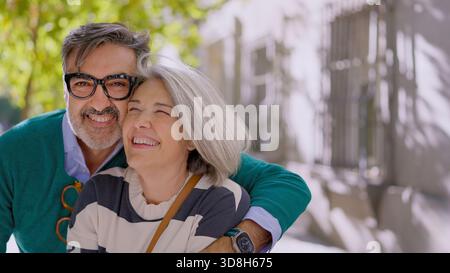 Couple senior aux cheveux gris souriant joyeusement dans la rue Banque D'Images