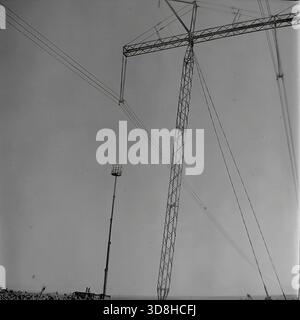 Région de Donetsk, RSS d'Ukraine, Union soviétique. 1970s. Une plate-forme de travail aérienne télescopique unique atteint une hauteur vertigineuse lors de la maintenance d’une ligne électrique à haute tension de 750 kV. La nacelle de l'ascenseur est positionnée près des conducteurs d'une tour massive de transmission à portail sécurisé par des haubans. Le mât élancé de l'ascenseur hydraulique contraste avec la structure en treillis métallique lourde du pylône. Une scène de machinerie spécialisée opérant dans la steppe. La vie dans le Donbass pacifique avant la guerre. Banque D'Images