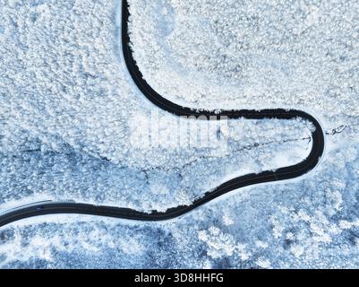 Vue de dessus de la route vide le long de la forêt d'hiver après les chutes de neige. Vue aérienne d'une route sinueuse à travers des arbres couverts de neige Banque D'Images