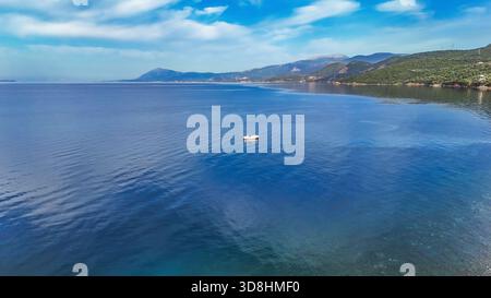 Vue aérienne par drone d'un petit bateau blanc avec une seule personne ramant lentement au petit matin près du village de Skaloma, dans le golfe de Corinthe. Banque D'Images