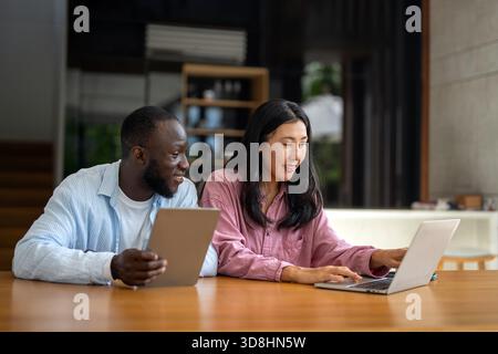 Équipe d'affaires, deux heureux divers, cadres multiethniques travaillant ensemble à l'aide d'un ordinateur portable dans le bureau. Banque D'Images