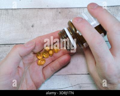 Verser des suppléments dans la main - gros plan des mains verser des capsules molles jaune vif d'une bouteille brune sur la paume, représentant la vitamine quotidienne Banque D'Images