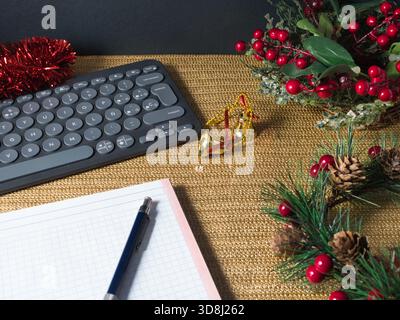Station de travail festive Holiday - clavier moderne, lunettes et un ordinateur portable sur une surface dorée chatoyante avec des décorations rouges de vacances, suggérant festiv Banque D'Images