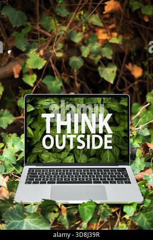 Ordinateur portable affichant du texte « Think Outside » sur son écran, entouré d'un feuillage vert luxuriant représentant la créativité, le travail indépendant à distance et la technologie écologique Banque D'Images