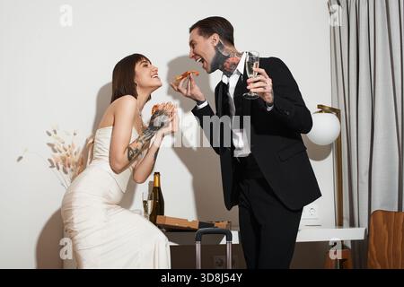 Un jeune couple profite de son moment privilégié dans un hôtel, riant et partageant une pizza. Banque D'Images