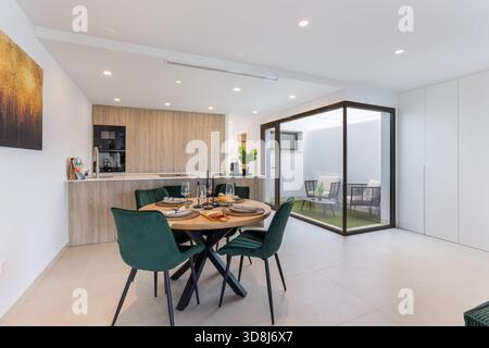 Salle à manger élégante avec chaises en velours vert, cuisine en bois et patio fermé avec meubles. Banque D'Images