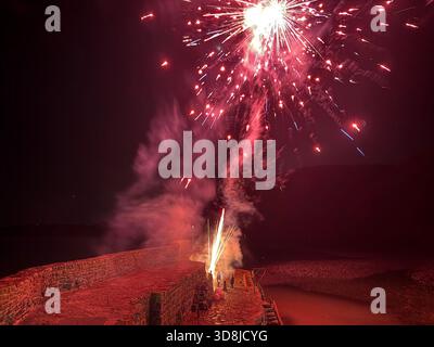 Des feux d'artifice illuminent le ciel nocturne au-dessus du port de Clovelly pendant l'allumage de la lumière de Noël RNLI dans le village de pêcheurs historique du Devon. Banque D'Images
