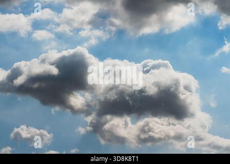 Le soleil caché derrière une masse de nuages gris foncé, avec des rayons de lumière et des ombres sur le ciel bleu, pour le fond Banque D'Images