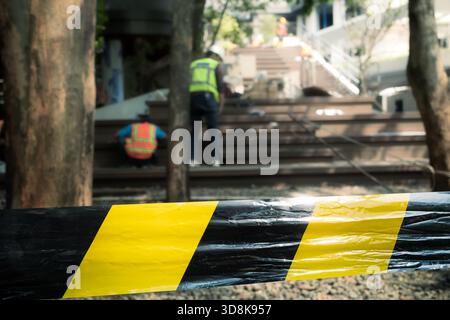 Une ligne de sécurité rayée noire et jaune s'étendait autour de la zone de rénovation du bâtiment avec des ouvriers de la construction en arrière-plan Banque D'Images