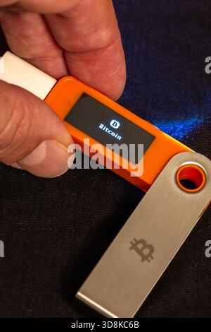 Main caucasienne tenant le portefeuille matériel Bitcoin. Confiance avec lumière artificielle en toile de fond. Banque D'Images